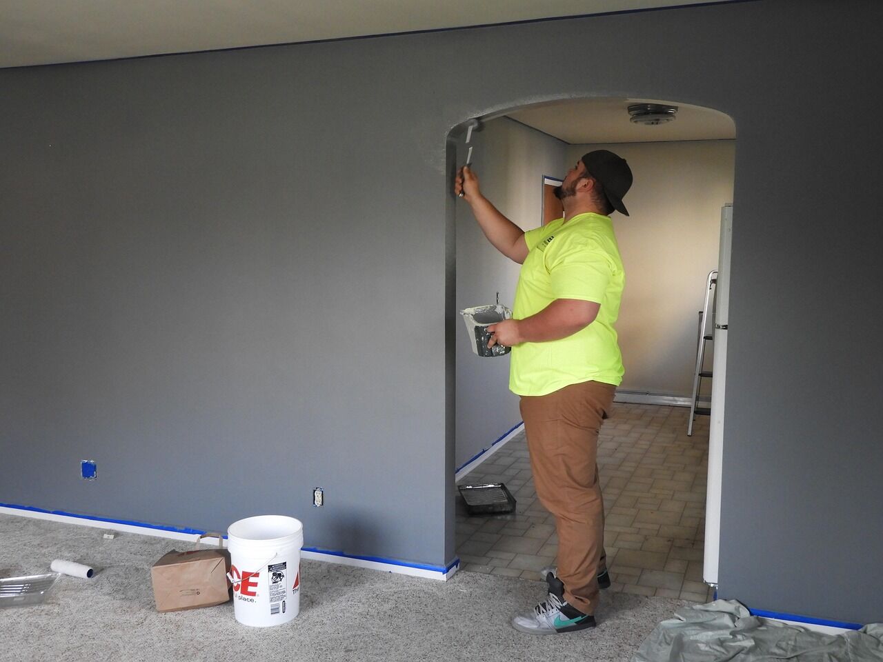 Pintor trabajando con brocha en una pared gris junto a un arco