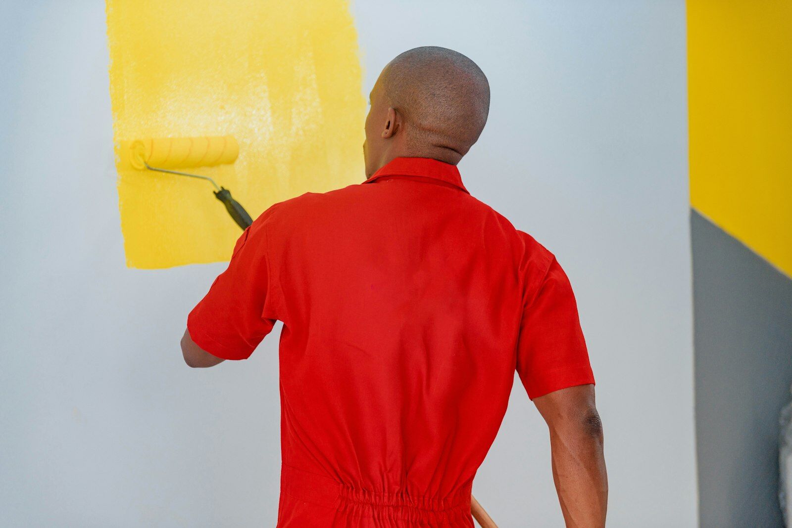 Pintor con rodillo aplicando pintura amarilla sobre una pared blanca