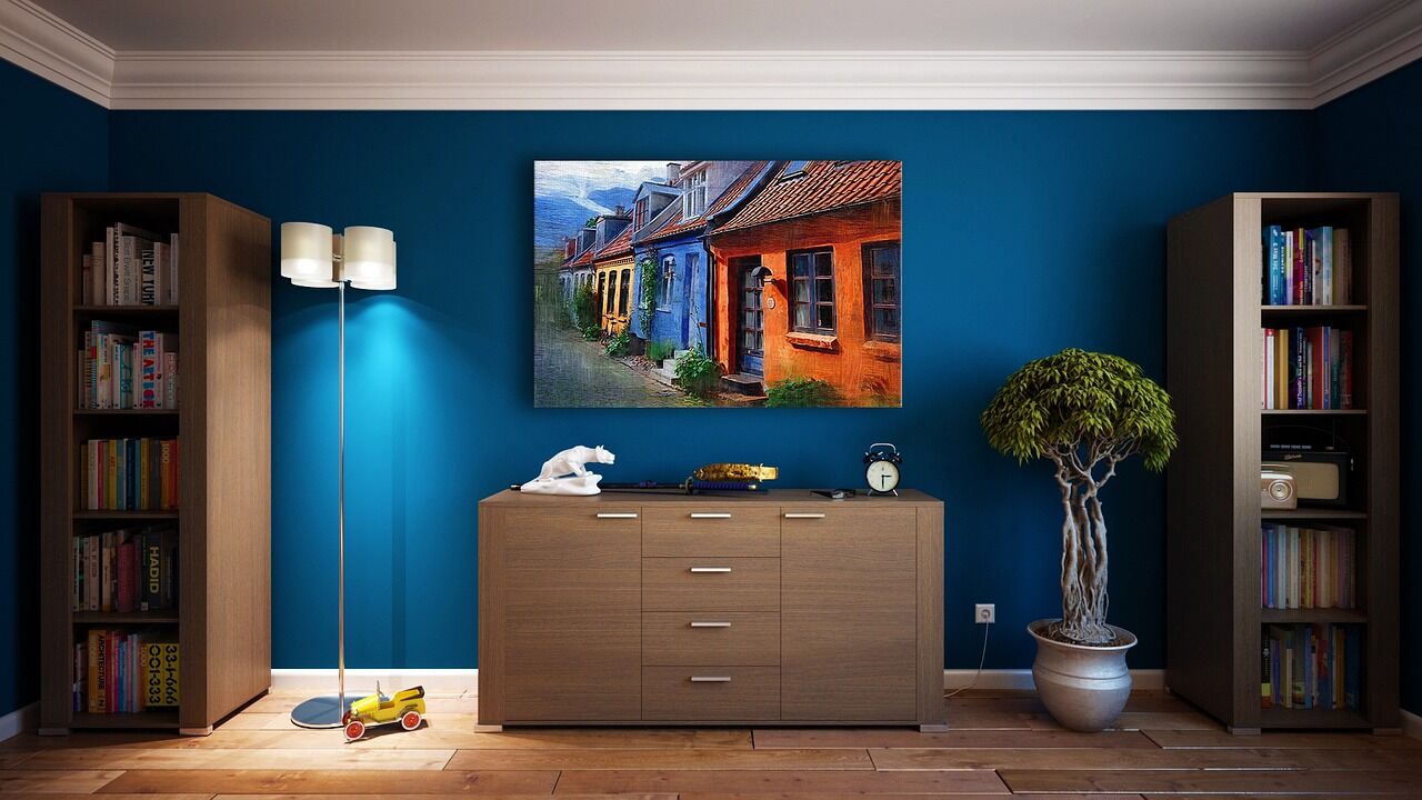 Sala con pared azul profundo, mueble de madera y un cuadro de casas de colores